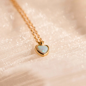 Detail of pink heart opal pendant on a delicate gold chain over silk background