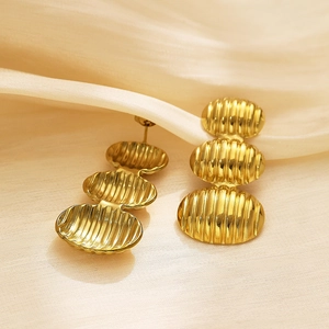Vue macro des boucles d'oreilles ovales dorées à trois couches sur tissu de soie