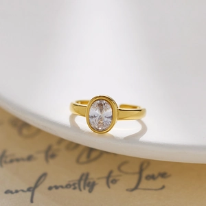 Close-up of gold oval crystal ring leaning on white porcelain for a romantic gift vibe