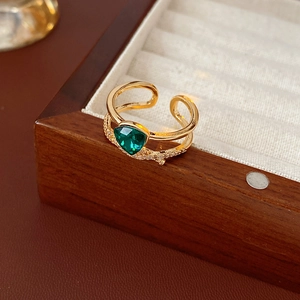 Détail d'une bague dorée croisée avec une gemme verte et des accents de zircon
