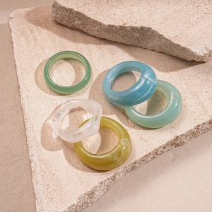 Close-up of geometric acrylic resin rings in green and blue on a textured stone base