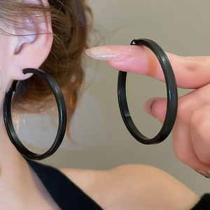 Close-up showing the size of large black geometric round hoop earrings on a model's ear