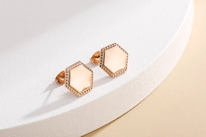 Detail of rose gold hexagonal stud earrings with fine beaded texture on smooth metal surface