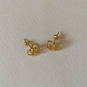 Close-up of golden knotted ball stud earrings in 925 silver on white textured surface
