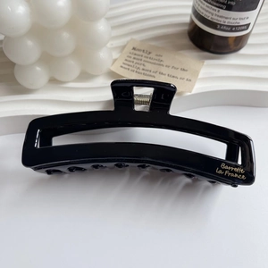 Detailed view of a black glossy hair claw clip with golden lettering on a white tray