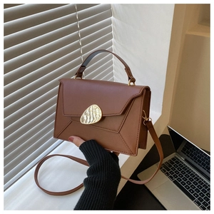 Close-up of brown leather handbag featuring a unique gold irregular clasp and top handle