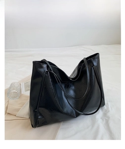 Detail view of large black tote bag in glossy leather on white aesthetic background