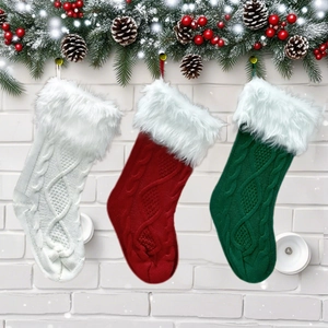 Three knit Christmas stockings in red white and green hanging on a white brick wall