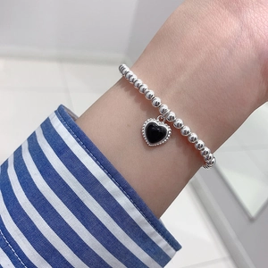 French vintage style silver beaded bracelet with a black heart charm on female wrist