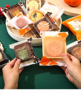 Macro shot of assorted mooncakes in printed plastic packaging held by hands for Moon Festival
