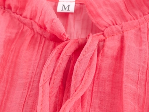 Close-up of pink pleated shirt neckline with size M tag and drawstring texture detail