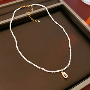 Detail of bohemian necklace with white seed beads and a gold shell pendant on a tray
