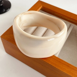 Macro view of minimalist creamy white acrylic bangle with marble pattern on a stand