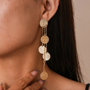 Detail of layered gold tassel earrings with textured circular discs on female model
