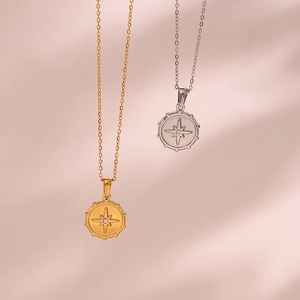 Close-up of gold and silver compass necklaces with zircons on a pink background