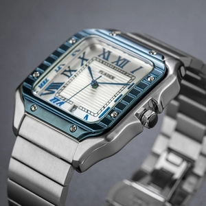 Detail view of square silver watch with blue bezel, roman numerals and calendar window