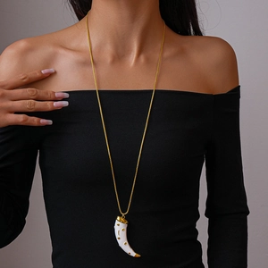 Detail of a gold-tone horn pendant necklace with white enamel inlay on a female model