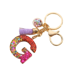 Colorful glitter resin letter G keychain with purple tassel and sequin ball on white background