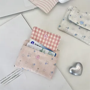 Détail d'un porte-cartes en toile florale avec fermeture à pression et doublure à carreaux