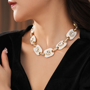 Gros plan d'un collier vintage doré avec maillons en émail blanc et cristaux sur un mannequin