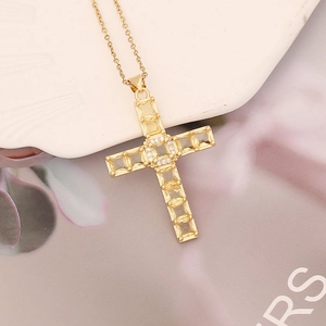 Detail shot of a golden cross pendant with zircon stones on a white ceramic stand