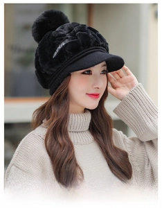 Detail of black plush knit hat featuring a decorative pom-pom and white embroidery text