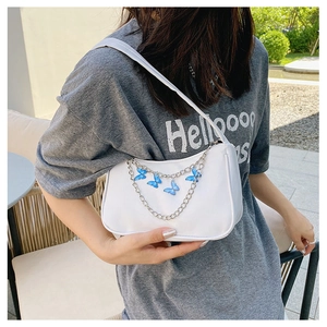 Detailed shot of white underarm bag featuring a silver chain with blue butterfly charms