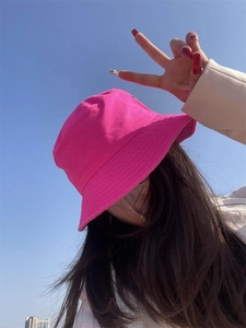Pink bucket hat made of fabric worn by a model against a clear blue sky background