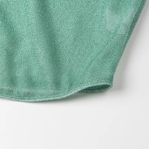 Détail du tissu scintillant vert menthe avec bordure en plumes sur l'ourlet de chemise