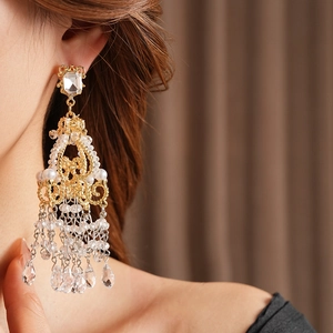 Detail of luxury gold tassel earrings with crystals and pearls worn by a model
