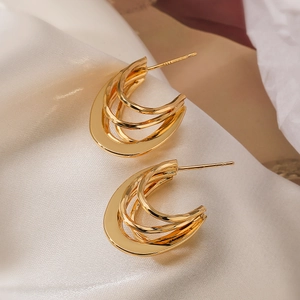 Detailaufnahme mehrlagiger goldener C-Form Creolen auf weichem Seidenstoff mit Glanz