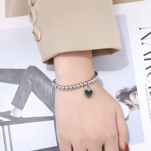 Bracelet à perles argentées avec breloque cœur noir porté par un mannequin élégant