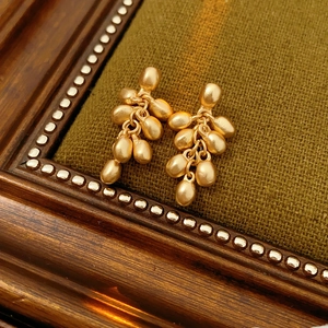 Close-up of matte gold beaded tassel earrings on deep green velvet vintage background