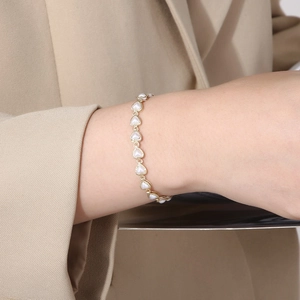 Close-up of minimalist gold heart and pearl link bracelet worn on a woman's wrist
