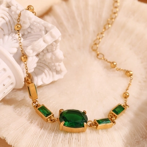 Macro view of 18K gold plated chain with oval emerald stone on a shell background