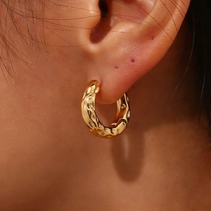Chic golden hoop earrings with irregular lunar texture worn on ear in a side view