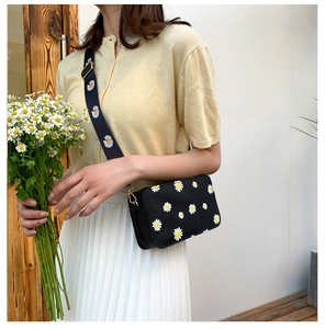 Side view of a black floral crossbody bag featuring daisy prints and a wide strap
