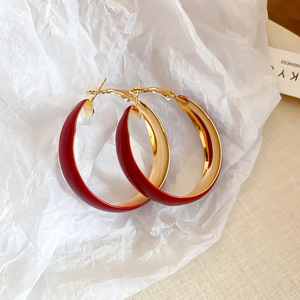 Close-up of oversized red and gold hoop earrings on textured white paper background