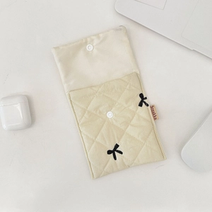 Close-up of beige quilted makeup bag with black bow embroidery and snap button closure