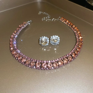 Detail of pink crystal necklace and clear stud earrings on a golden reflective surface
