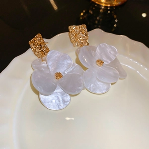 Detail of acrylic flower earrings with golden textured metal square studs on white ceramic plate