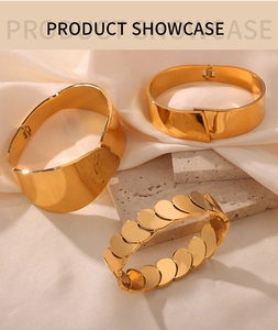 Detailed view of three minimalist gold polished bracelets on white silk and stone texture