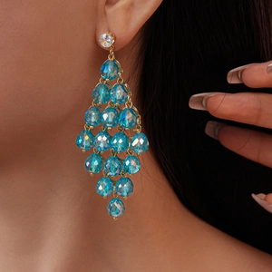 Close-up of elegant gold earrings with faceted blue crystal beads on a model