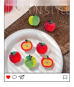 Detail of cute red and green resin apple hair clips on a white ceramic plate