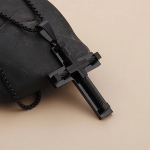 Close-up of black titanium steel cross pendant with woven texture on dark stone