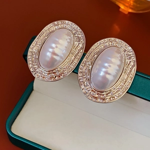 Macro detail of oval pearl earrings with gold rippled metal frame on a green jewelry box
