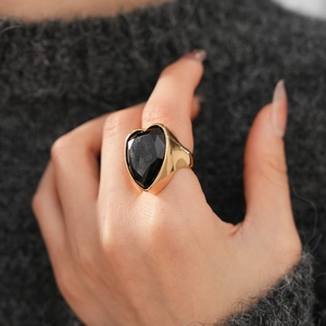 Detailed view of wide gold band ring featuring a large faceted heart-shaped black gemstone