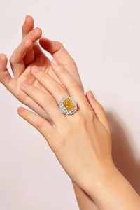 Close-up of model wearing a rectangle yellow stone ring with cluster diamond halo