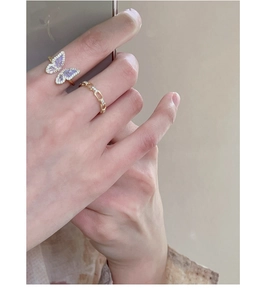 Macro detail of a purple butterfly ring with gold edging and a gold chain ring on a finger