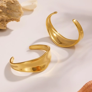 Detalle de dos brazaletes dorados anchos con acabado pulido y diseño de ondas fluidas